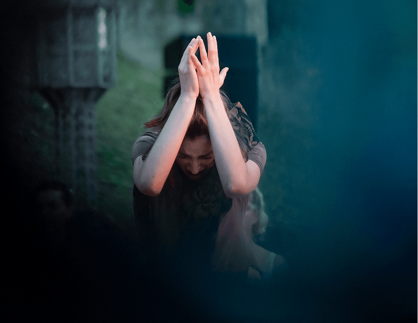 Actress expressing deep emotion with hands clasped above her head during a sensory-sensitive scene in Flute Theatre’s Shakespeare production.